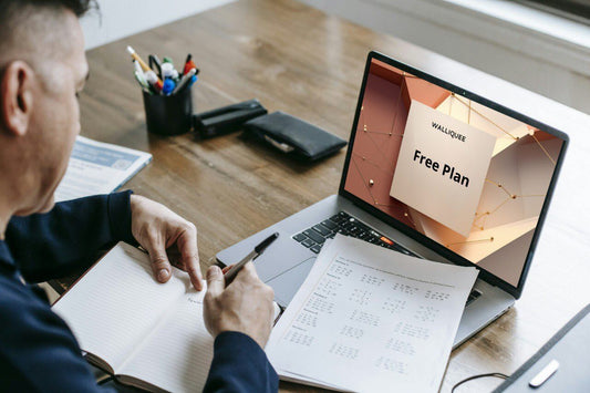 Person working at a desk with a laptop displaying a 'Free Plan' offer, surrounded by documents and stationery.